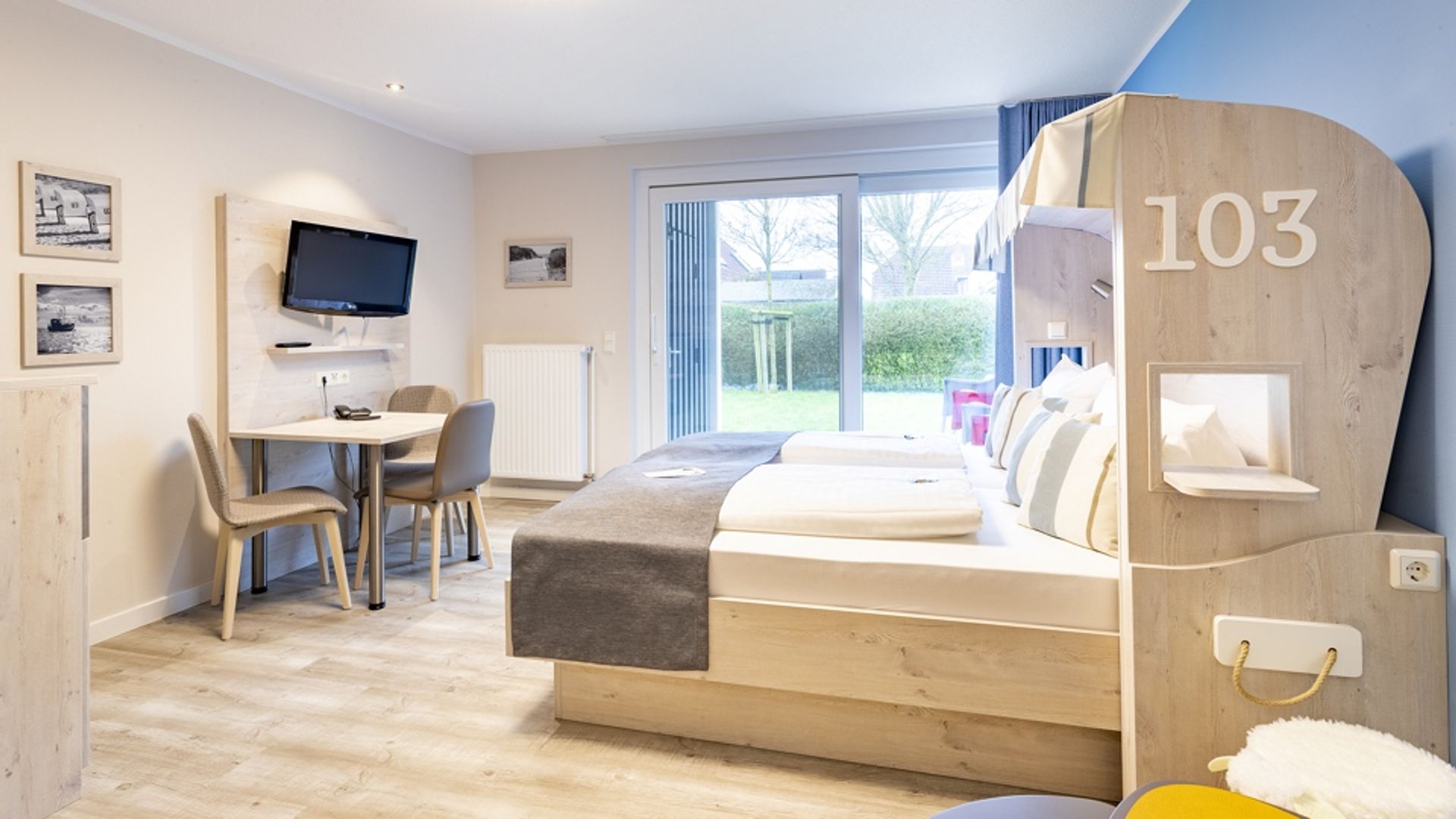 Links ist die Sitzecke mit Fernseher zu sehen, rechts das Doppelbett im Strandkorb-Stil