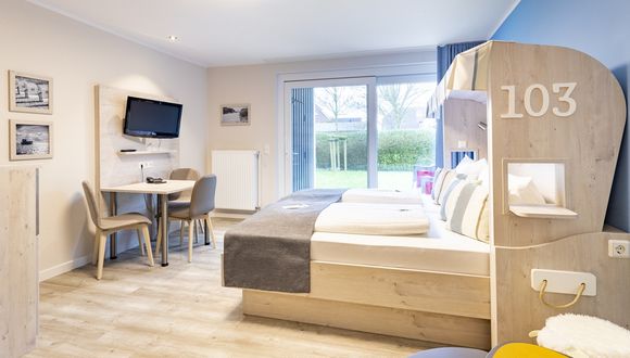 Links ist die Sitzecke mit Fernseher zu sehen, rechts das Doppelbett im Strandkorb-Stil