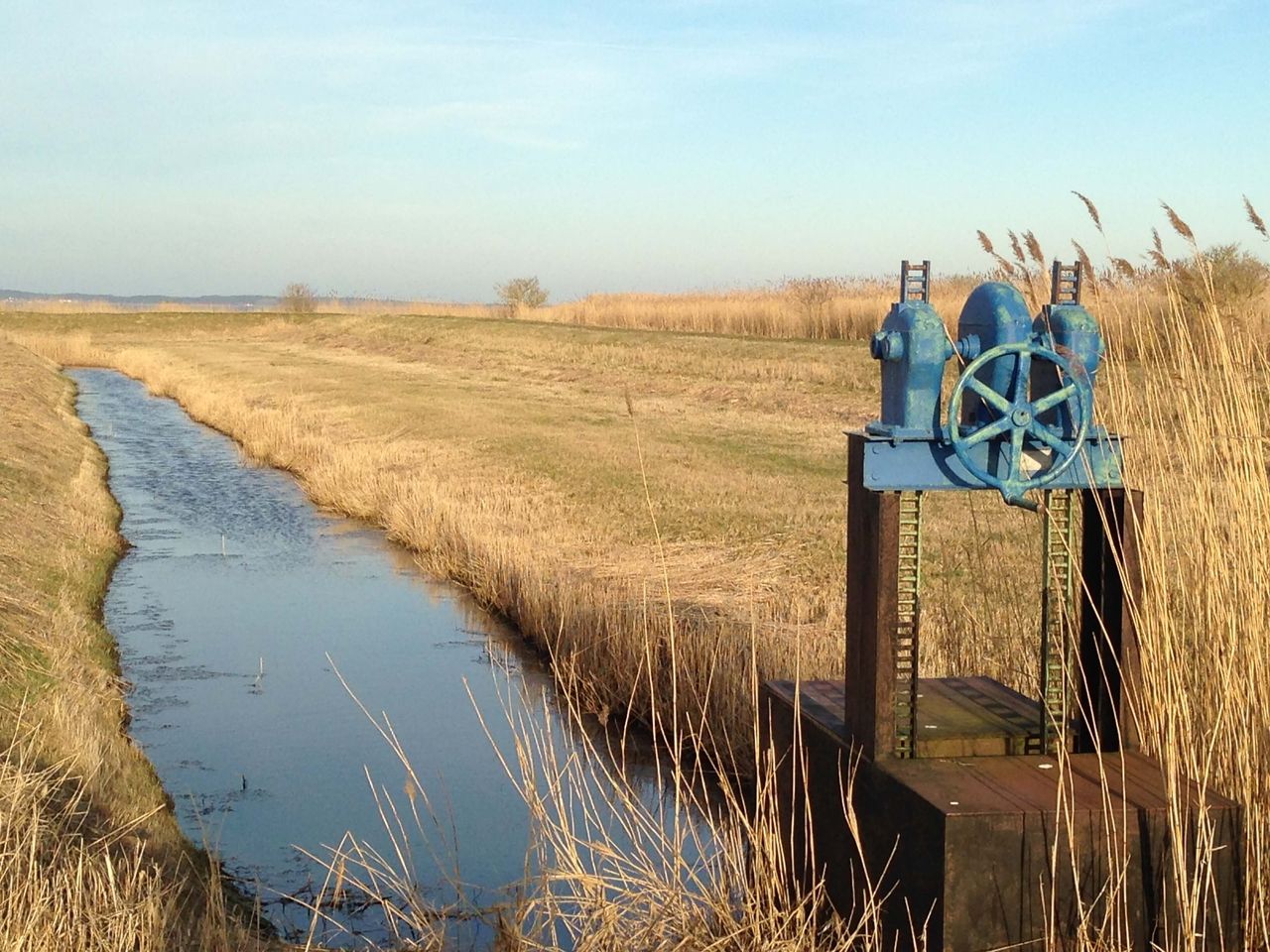Foto von einem Pumpwerk, welches sich an einem kleinen Kanal befindet, links und rechts sind Wiesen und Gräser zu sehen